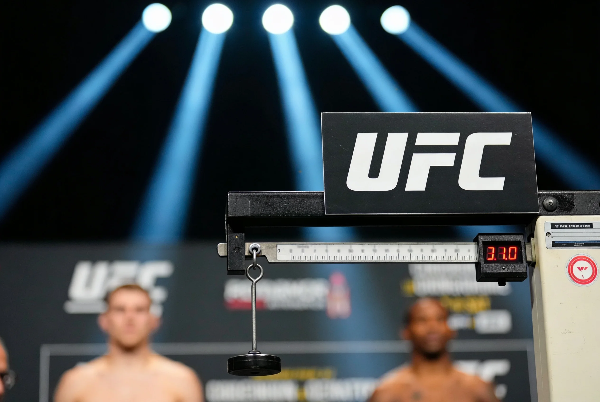 UFC weigh-in scale under bright lights with a digital display showing a weight reading